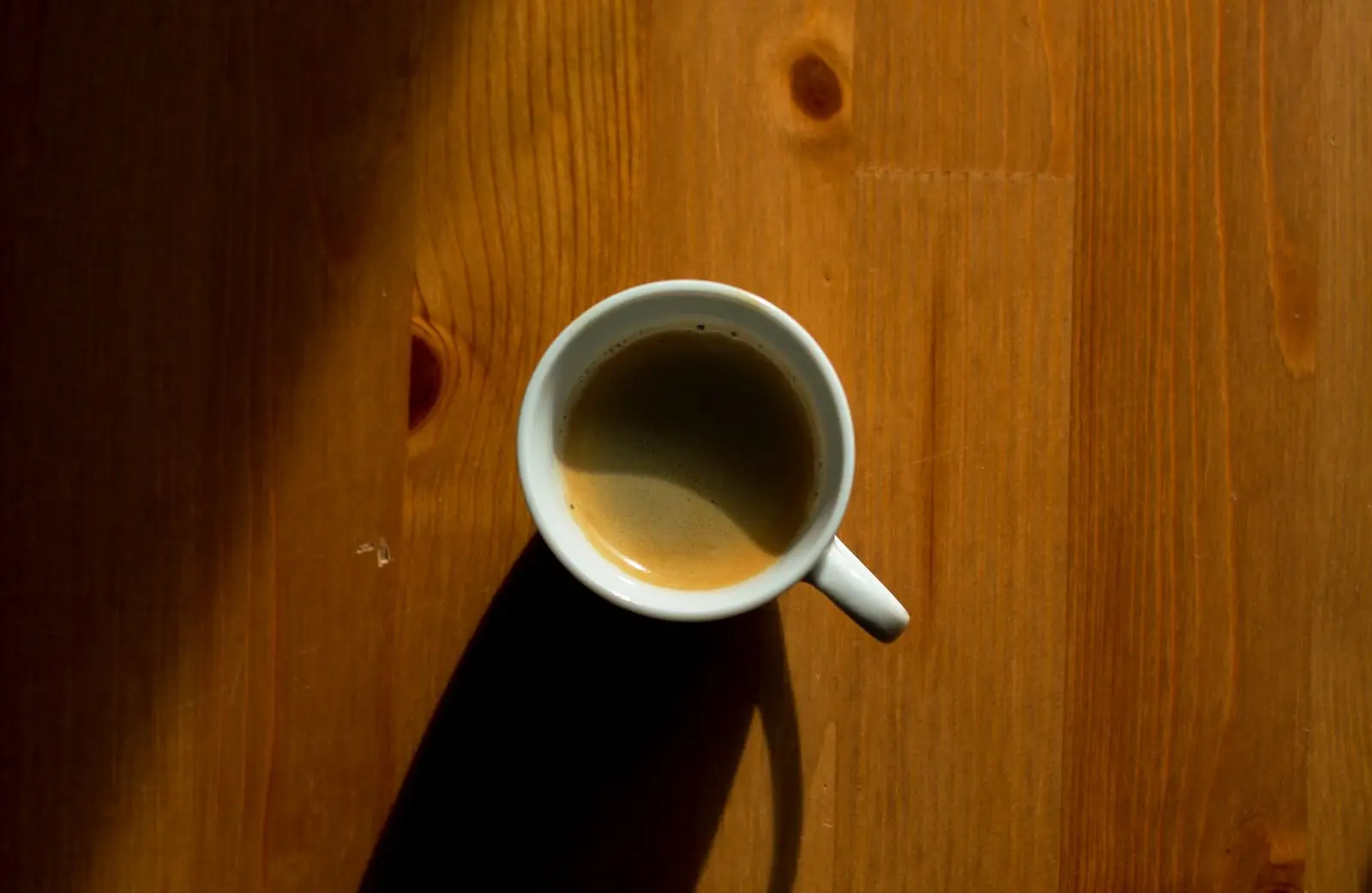 Cup of coffee casting a shadow on a wooden table