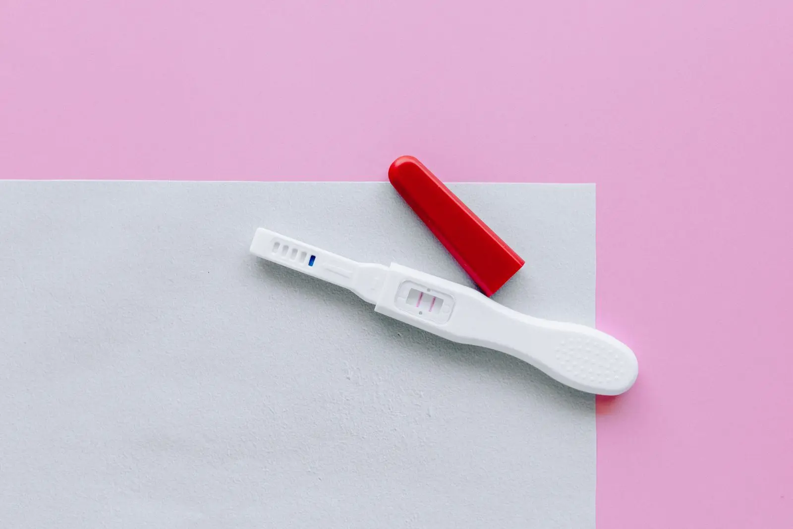 Home pregnancy test with a red cap lying on a pink and white surface