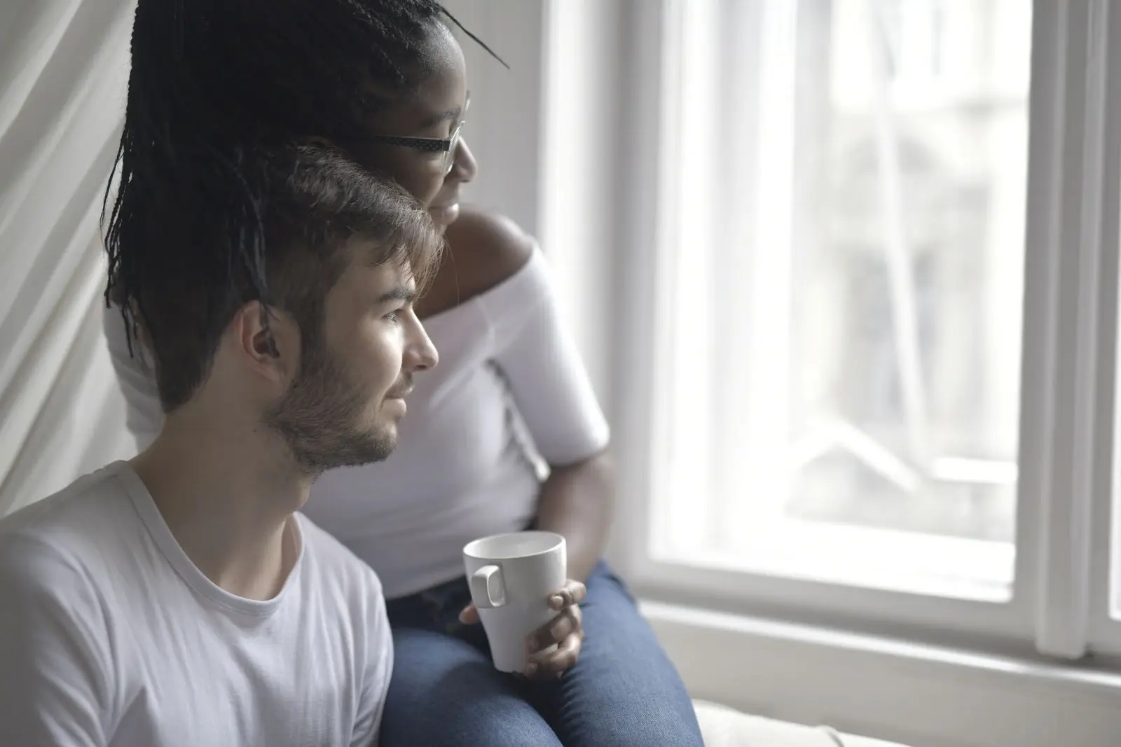 Couple sitting close together by a window with a cup of coffee