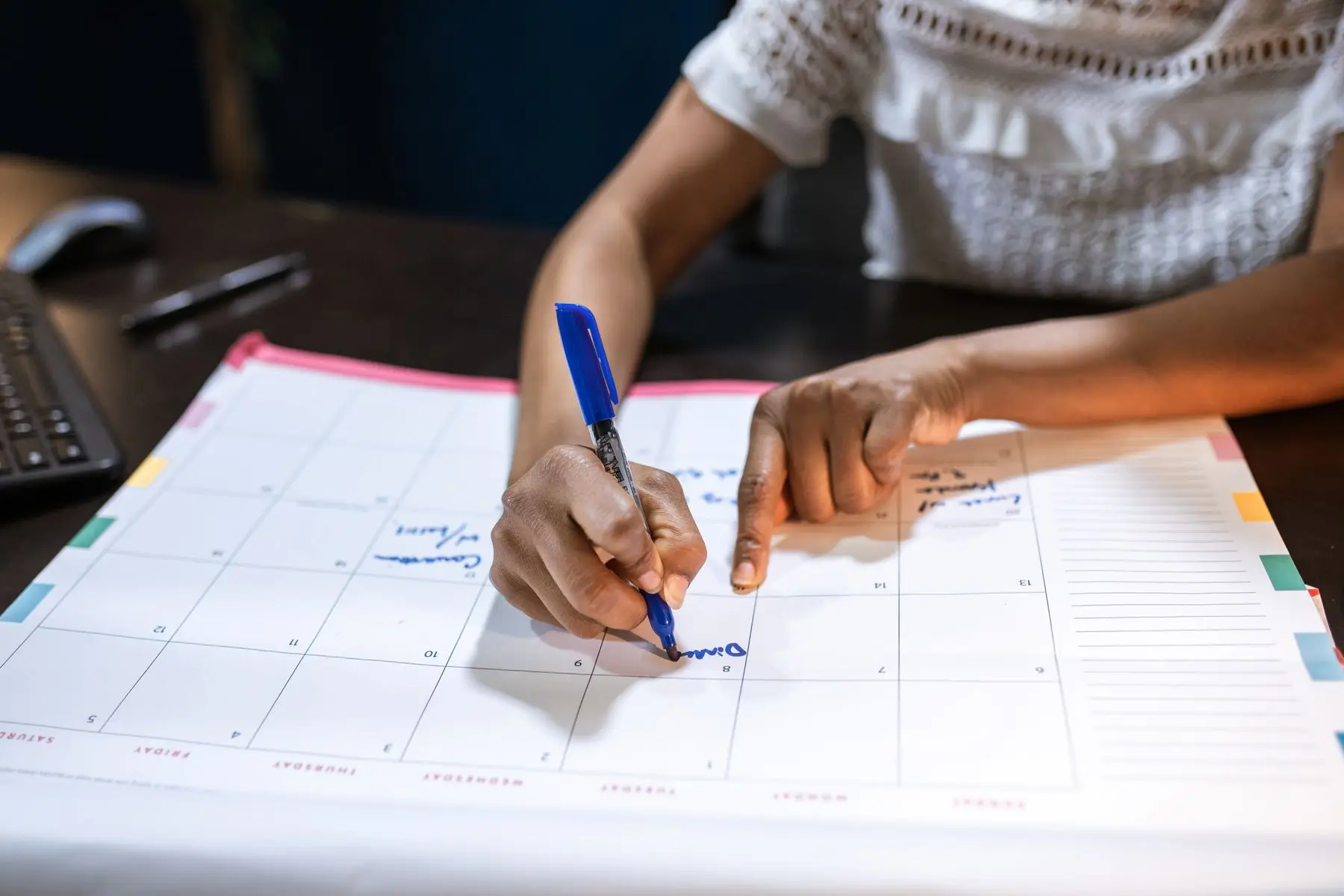 Woman writing on a paper wall-style calendar with a blue pen to mark important dates