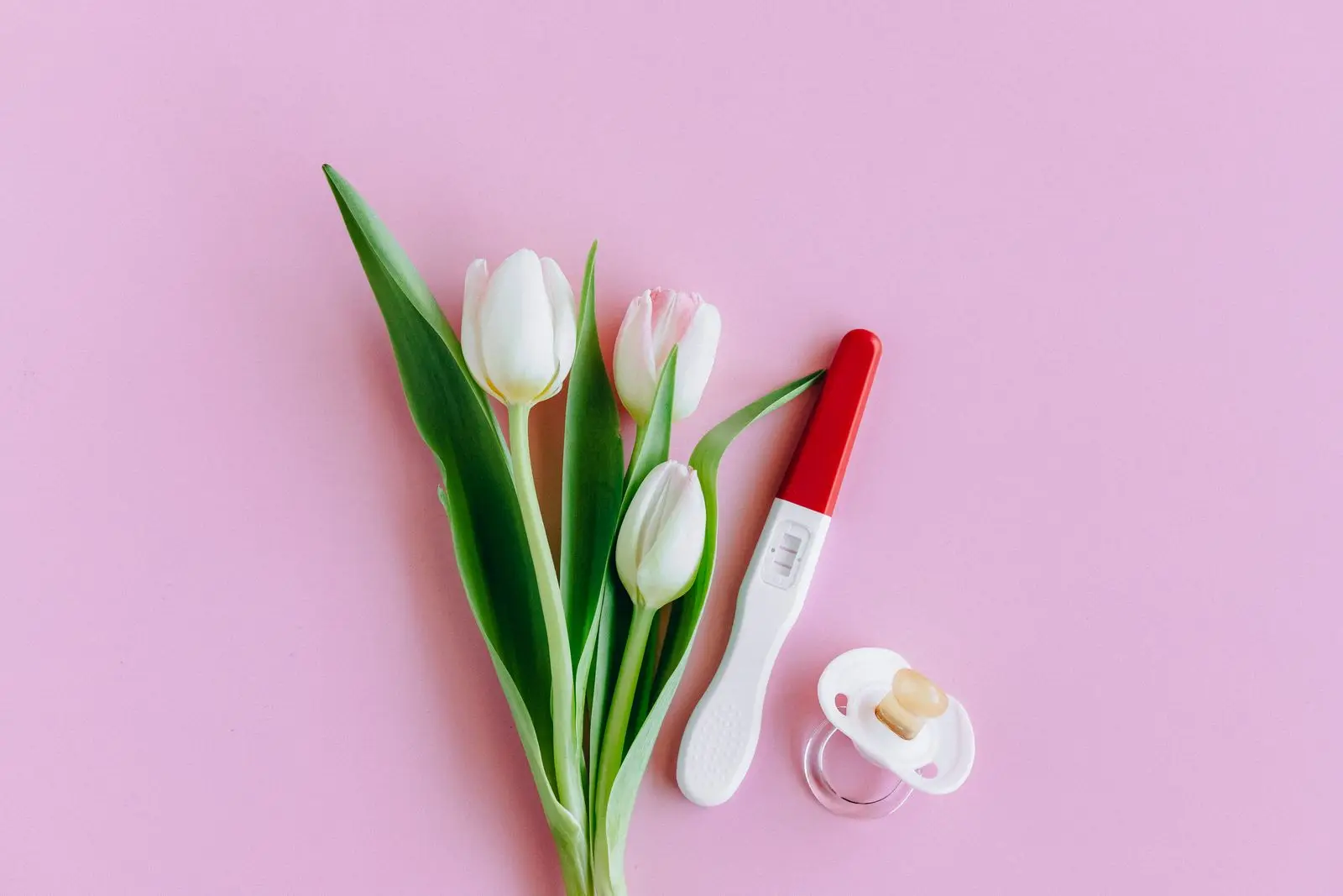 Pink tulips, a pregnancy test and a pacifier on a soft pink surface