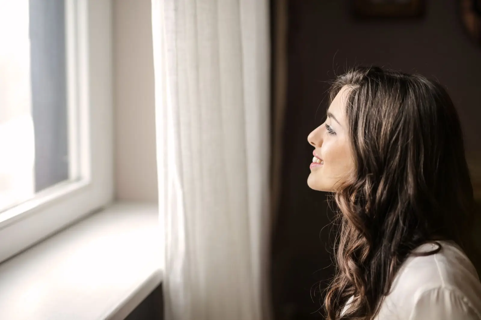 Smiling woman looking out of a window at home