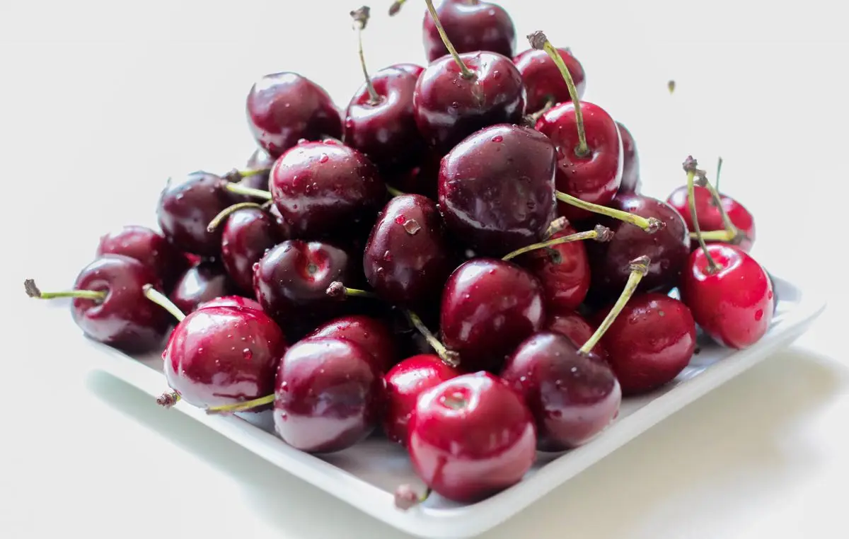 Fresh red cherries on a white plate, about the size of your baby at 9 weeks pregnant