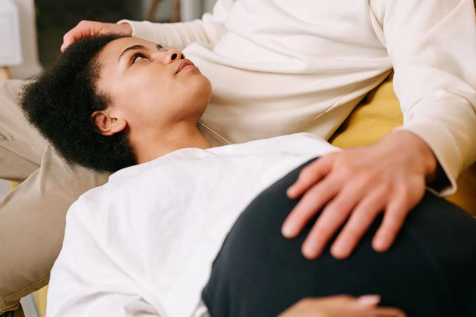 Expectant couple sharing a tender moment, with the pregnant woman resting on her partner's lap