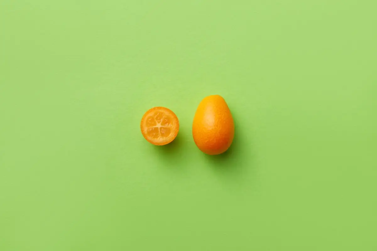 A whole kumquat and a halved kumquat on a green background, about the size of your baby at 10 weeks pregnant