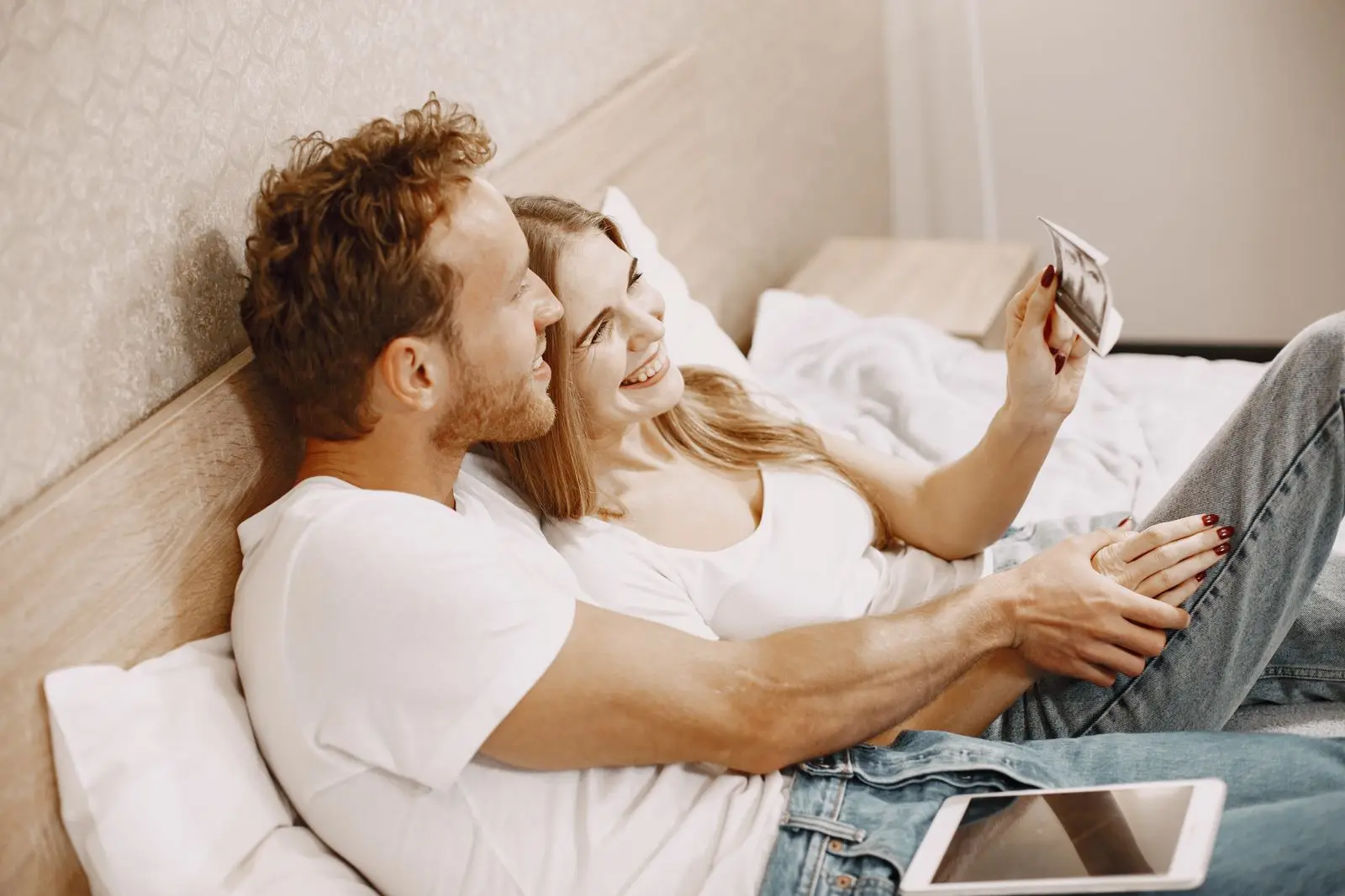 Happy couple lying on a bed holding their 12-week ultrasound scan