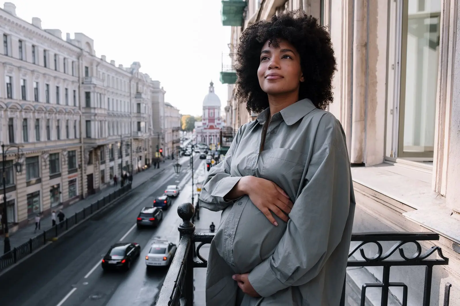 Pregnant woman standing on a balcony with her hand on her belly