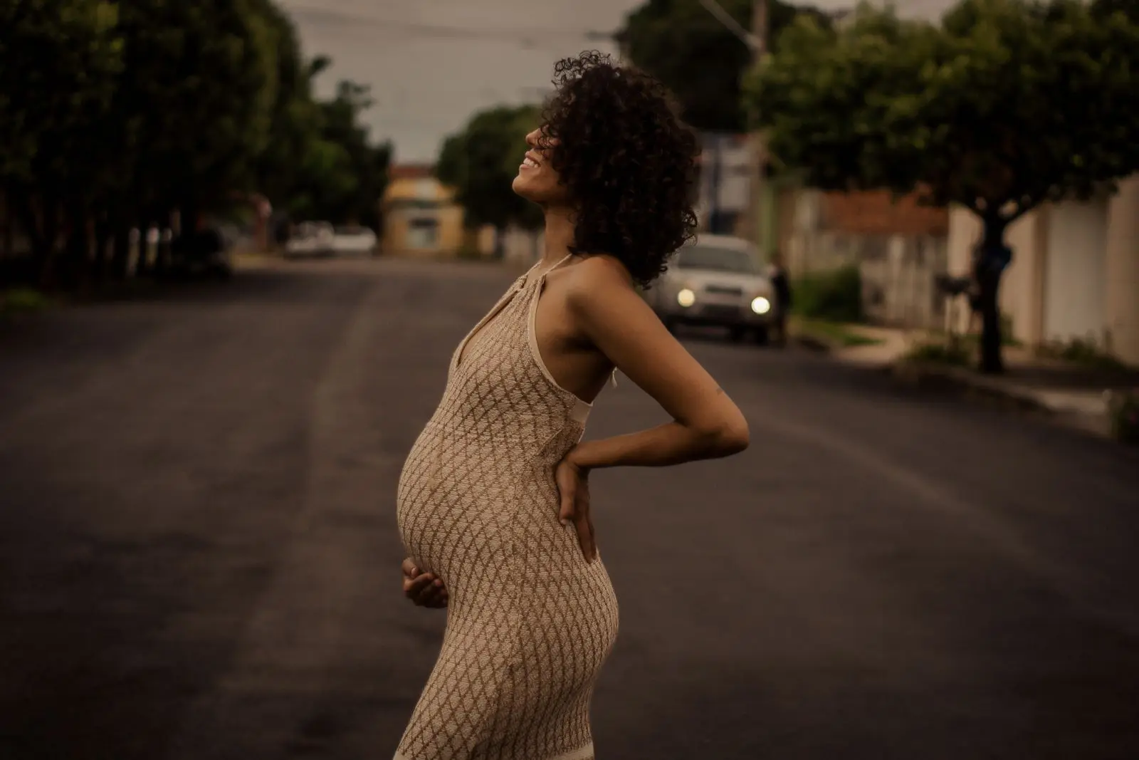 Smiling pregnant woman with curly hair standing outdoors