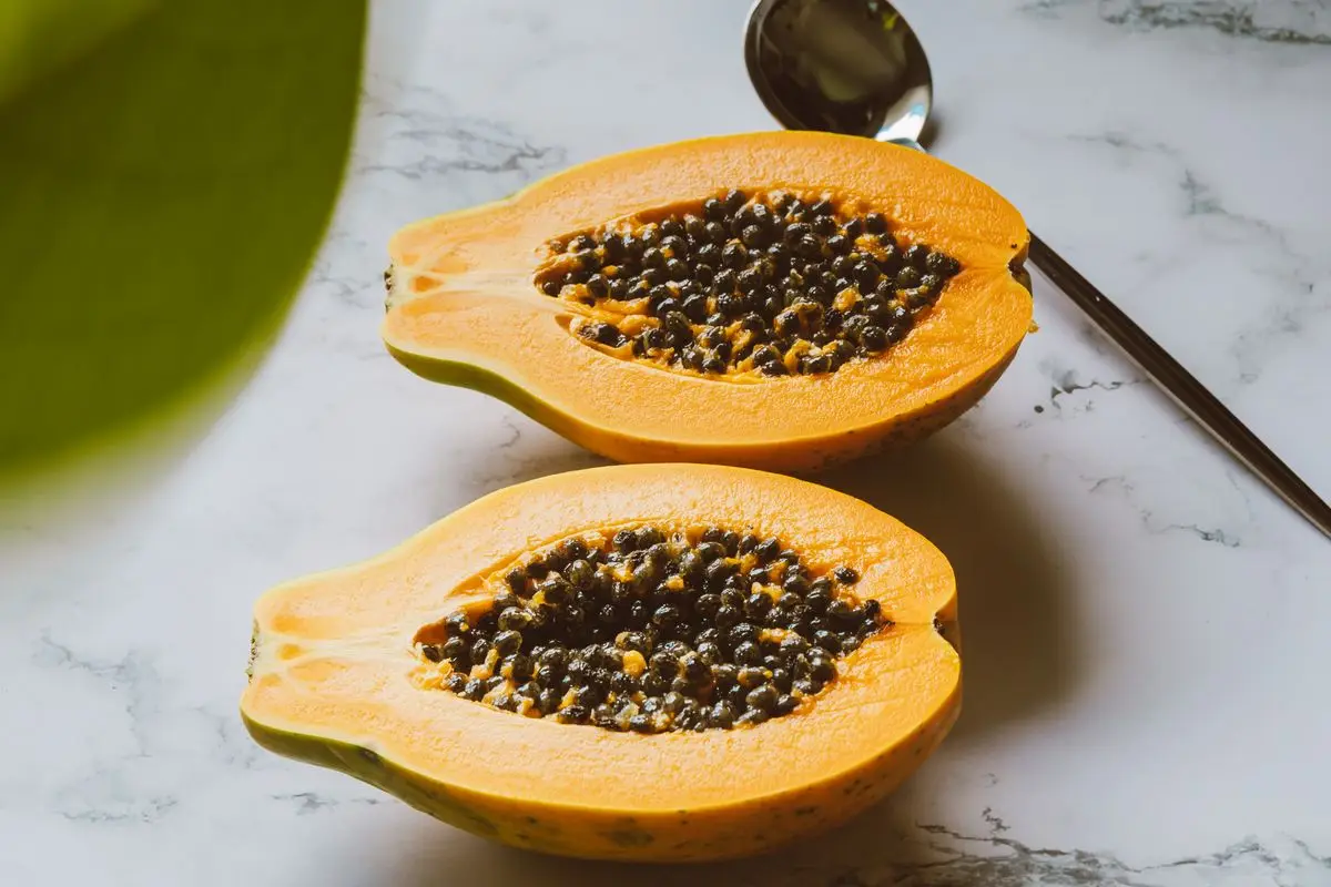 Two ripe papaya halves with black seeds on a white marble surface, about the size of your baby at 23 weeks pregnant