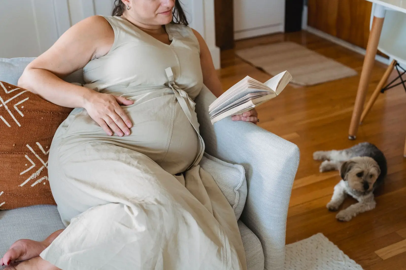 Pregnant woman resting on a couch reading a book with her dog nearby