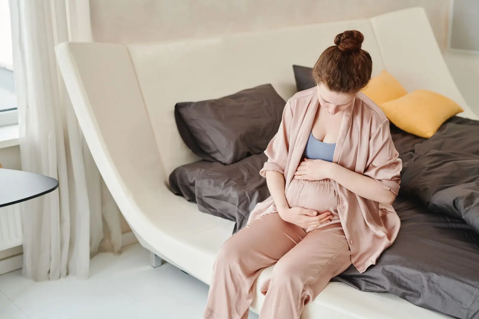 Pregnant woman sitting on a bed holding her belly during a tightening