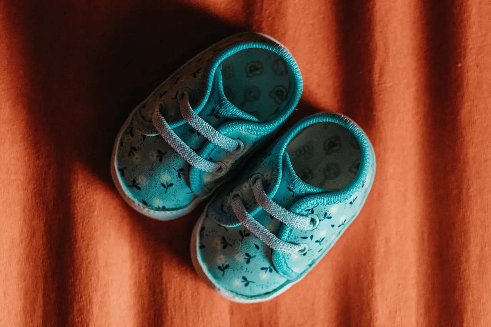 Pair of small blue baby shoes with a floral pattern on orange fabric