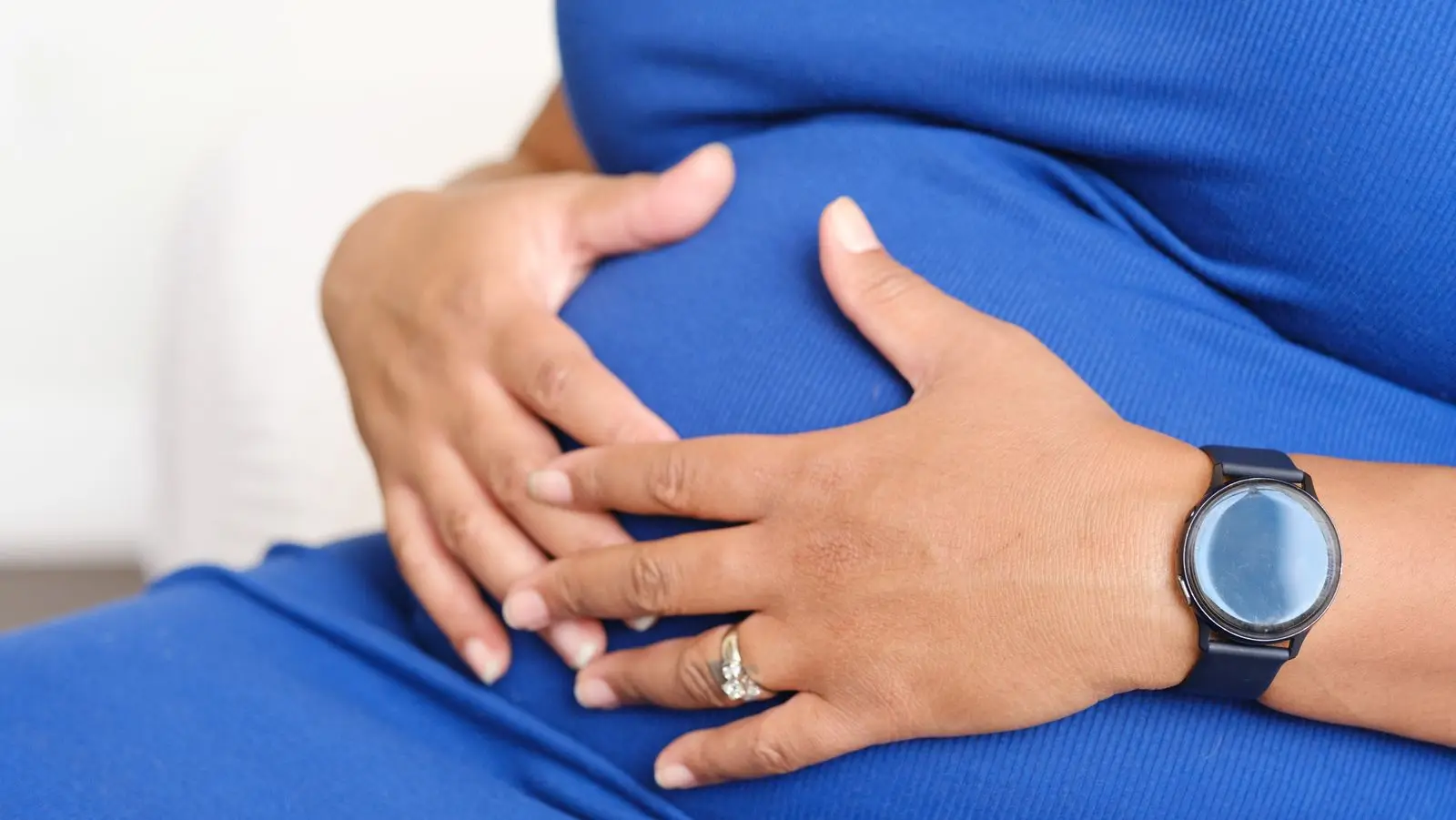 Pregnant woman resting her hands on her belly, wearing a watch to time contractions